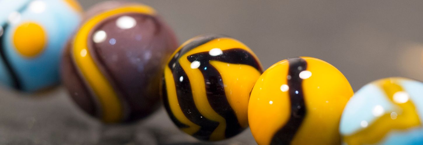 Alignement de perles d'art en verre filé aux motifs zébrés jaunes, noirs et bleus translucides.