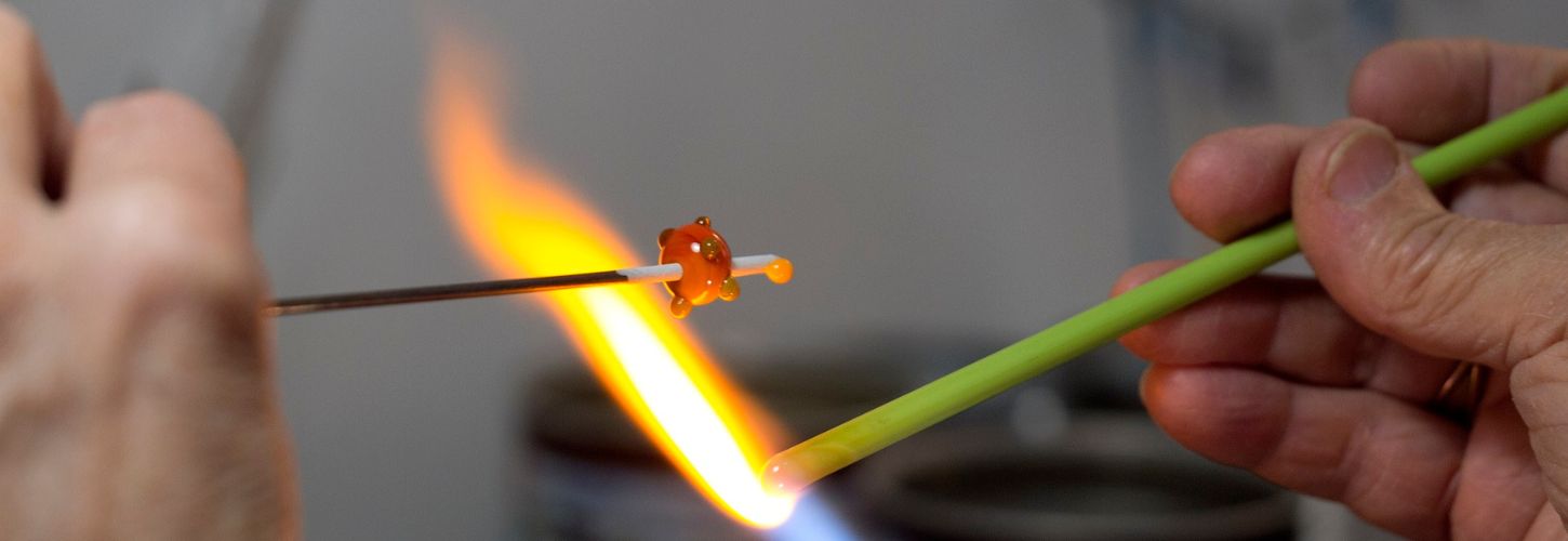 Application précise d'un point de verre en fusion orange sur une perle en cours de création au chalumeau.