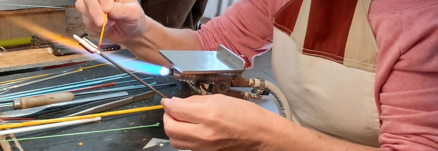 Gros plan sur le dépôt minutieux de verre en fusion jaune sur une perle d'art en cours de création.