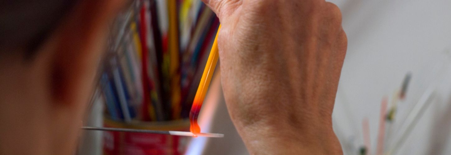 Artisane perlière faisant fondre l'extrémité d'une baguette de verre jaune clair au-dessus d'un outil de lissage.