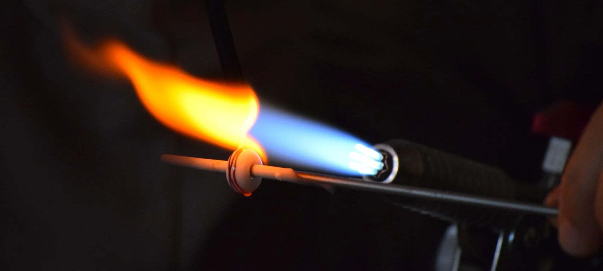 Perles d'art en verre au chalumeau Perle de verre décorée de points blancs en cours de lissage et de recuisson sous la flamme.