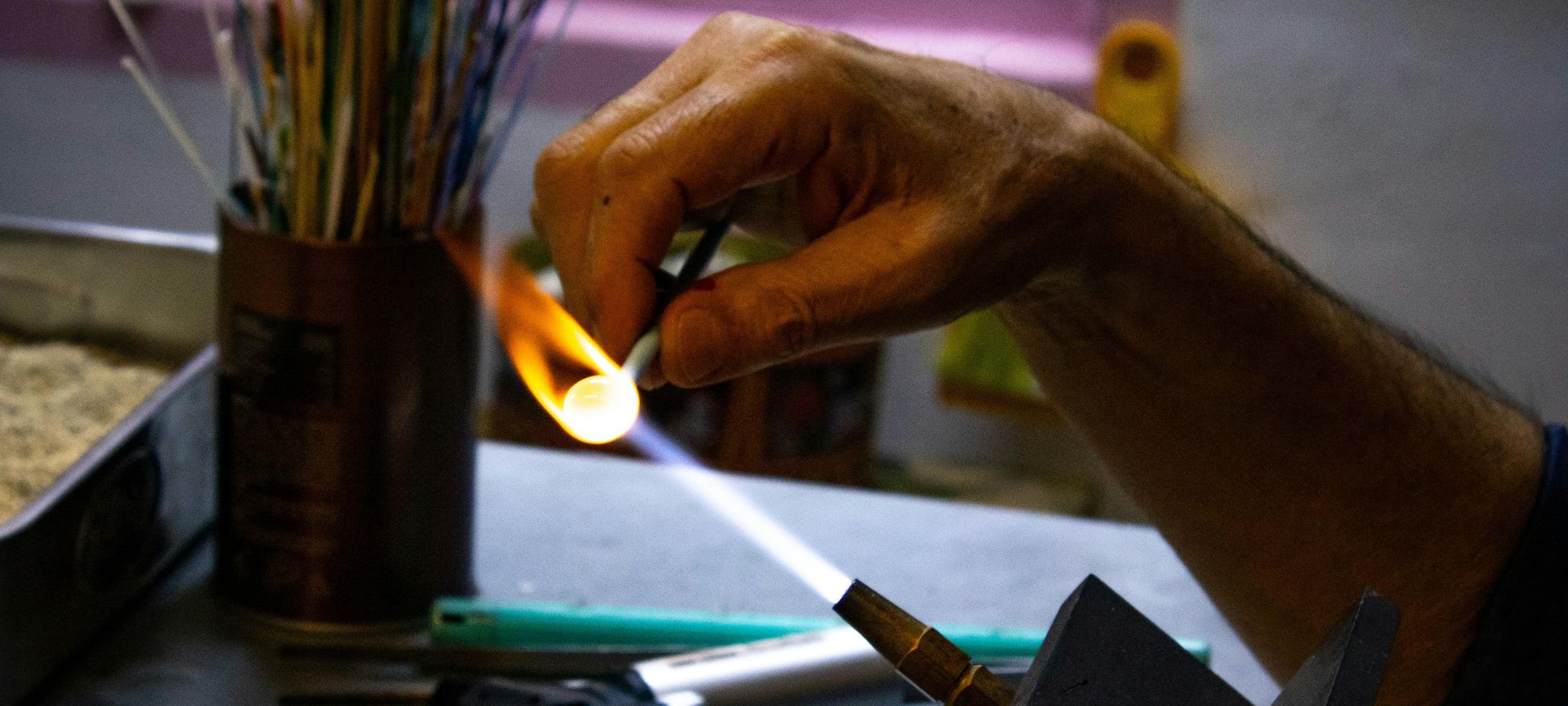 Fileuse de verre faisant tourner un mandrin sous la flamme d'un chalumeau de verrier.